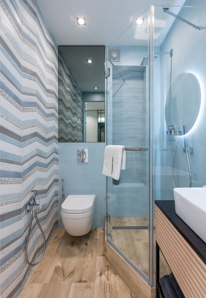 Interior of modern bright bathroom with toilet next to glass walls with shower near mirror on wall and sink on counter